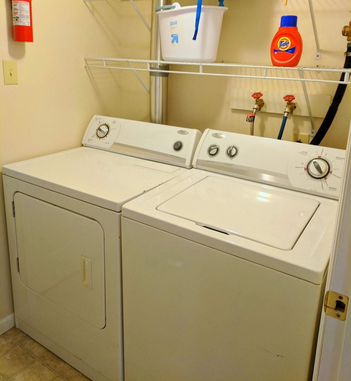 A laundry area with two front-loading washing machines, a white plastic laundry basket, and a Tide detergent bottle.