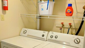Un área de lavandería con dos lavadoras de carga frontal, una cesta de plástico blanca y una botella de detergente Tide.