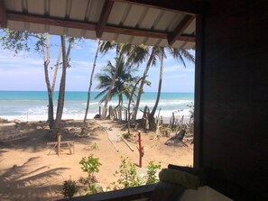 A beach view from a covered area with a wooden bench and a table, palm trees, and a sandy beach. - Authentic Beachfront Caribbean Hideaway-Crashing Surf, Palms, & Tradewinds! (Las Canas)