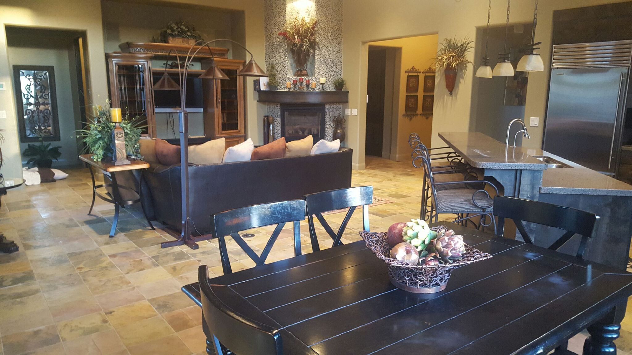 A dining area with a black table and chairs, a basket of fruits, and a fireplace with a stone wall behind it.
