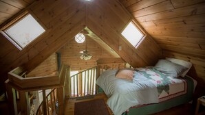 Un dormitorio acogedor en el ático, con techo inclinado, una cama con colcha y dos tragaluces.