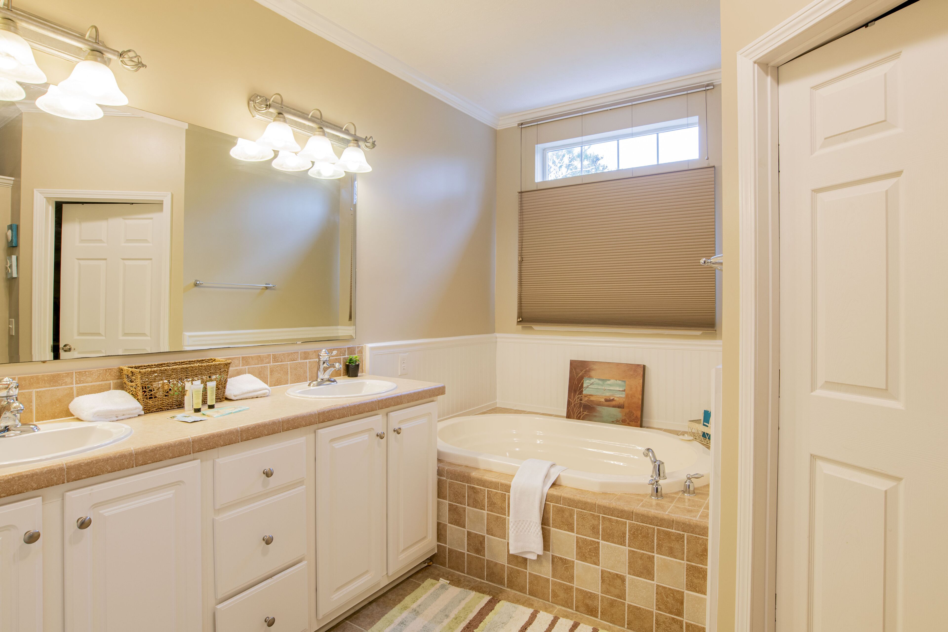 A bathroom with two sinks, a bathtub, a large mirror, and a window with blinds.