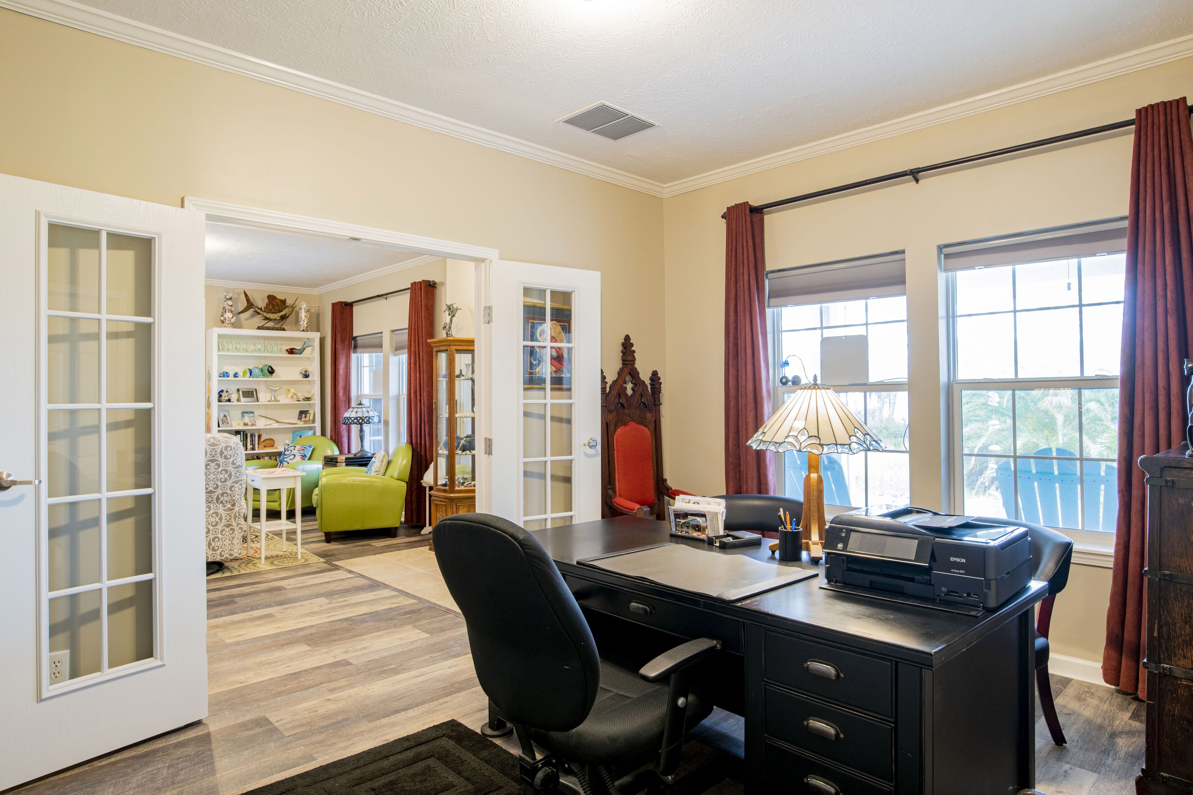A home office with a desk, printer, and a view of the outside through large windows.