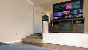 Un salon doté d’un téléviseur à écran plat fixé au mur, d’une cheminée et d’un escalier menant à une autre pièce.