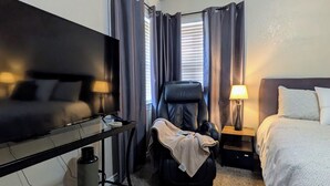 Une chambre d’hôtel équipée d’un lit, d’un fauteuil massant, d’une télévision, d’un bureau avec une lampe et d’une plante en pot.