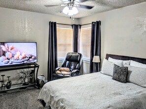 A hotel room with a bed, a chair, a TV, and a ceiling fan.