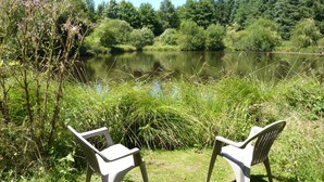 Two white plastic chairs facing a calm lake surrounded by lush greenery. - Peaceful Haven in Regional National Park with Private Lake (Dournazac)