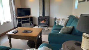 A cozy living room with a television, a wooden table, a sofa, and a fireplace. - Peaceful Haven in Regional National Park with Private Lake (Dournazac)