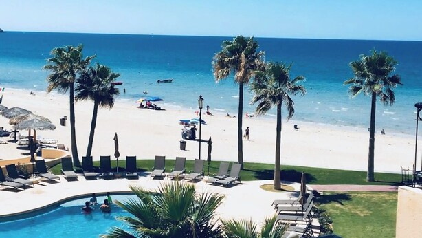 Een resort met een zwembad, strand en palmbomen.