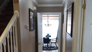 A hallway with a staircase, a dining area in the background, and a ceiling light.