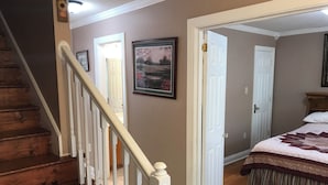 A bedroom with a wooden staircase, a bed with a quilt, and a door leading to another room.
