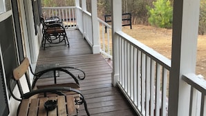 A covered porch with wooden benches and a railing, overlooking a wooded area.