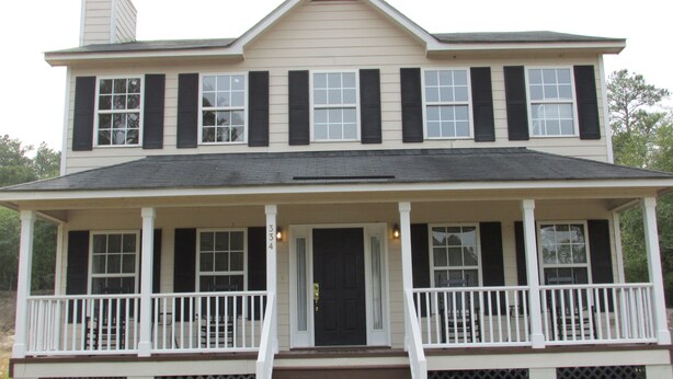A two-story house with a front porch, white railings, and a black door.