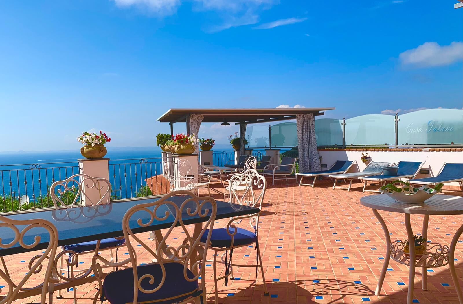 Eine Terrasse mit Tisch und Stühlen, einer Pergola und Lounge-Sesseln mit Blick aufs Meer.