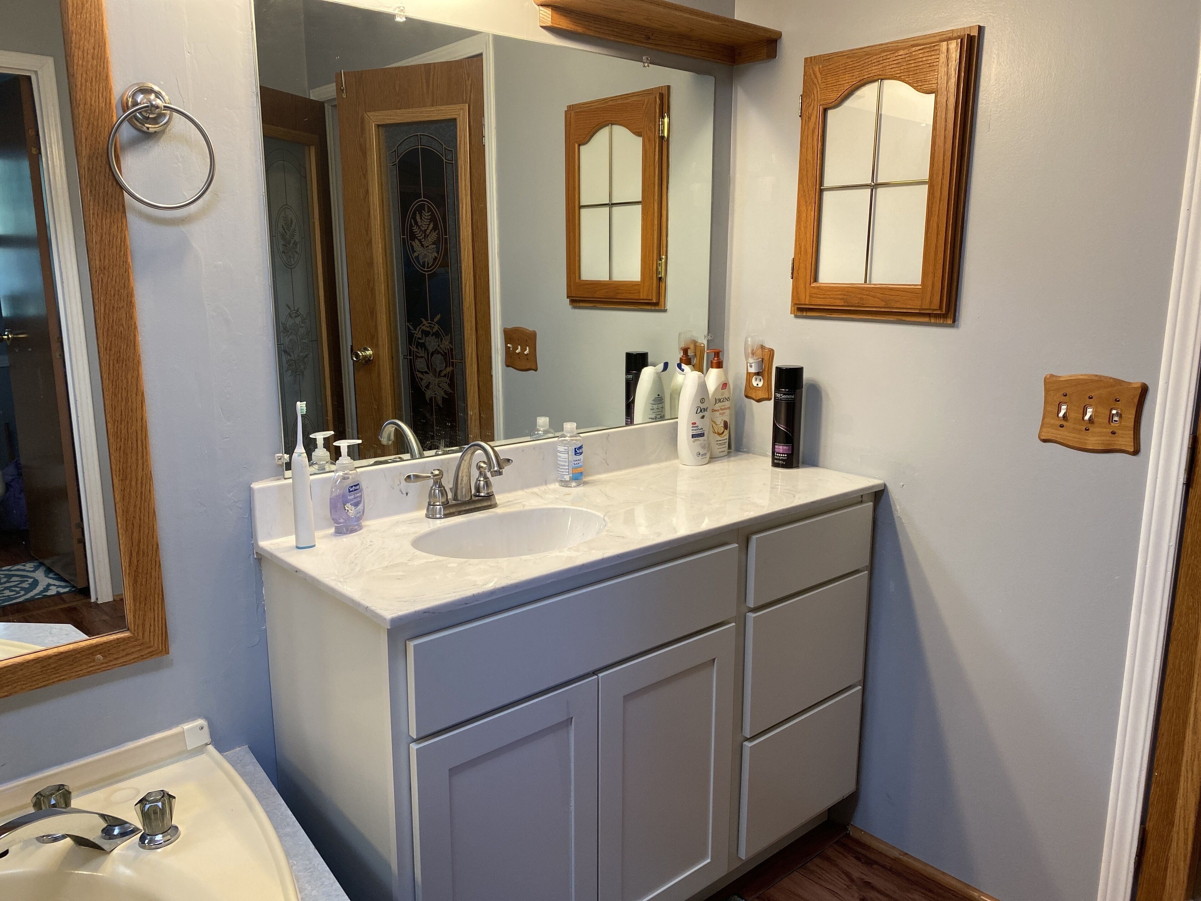 Un baño con un lavamanos blanco, dos espejos, marcos de puerta de madera y un armario de madera.
