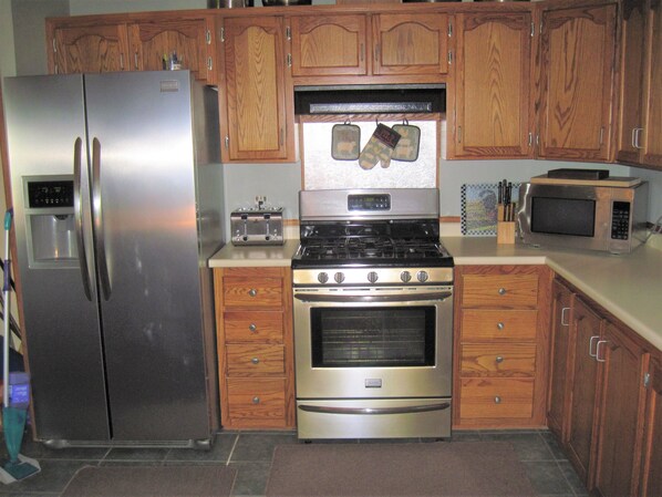 A kitchen with a stainless steel refrigerator, a stove, a microwave, wooden cabinets, and a water dispenser.