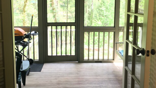 Eine Holzterrasse mit Blick auf einen Wald, ein Grill und eine Tür zum Innenbereich.