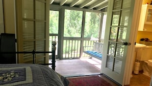 Ein Schlafzimmer mit einem Bett, Holzboden, einem roten Teppich und Blick auf eine Veranda mit einer Bank.