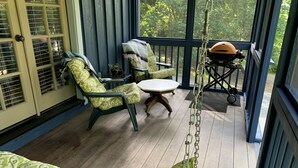Eine Veranda mit grün gemusterten Stühlen, einem kleinen Tisch und einem Grill.