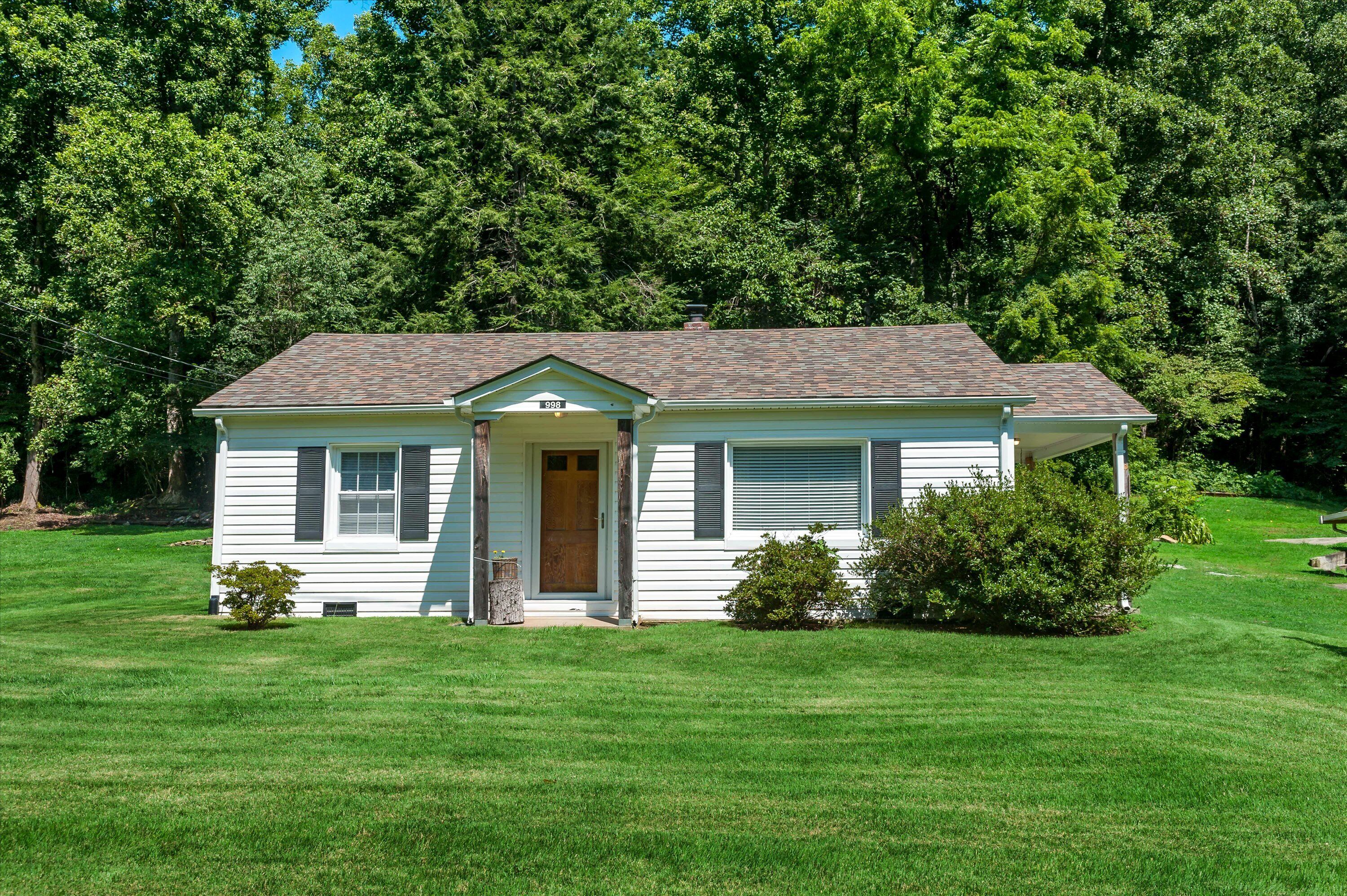 A single-story house with a front porch, a small front yard, and a wooded backdrop.