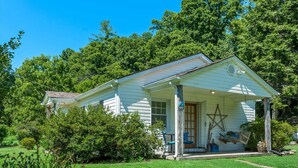 A white house with a porch, surrounded by lush greenery and trees. - Stay and Play @ Railway Rest, near AVL, trails, falls (Old Fort)