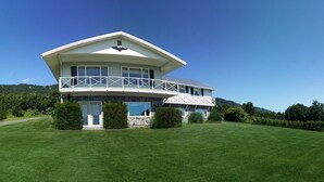A two-story house with a balcony, surrounded by a well-maintained lawn and trees. - Historic - Private 28 Acres - 180° Ocean View! - Carolyn's suite (Homer)