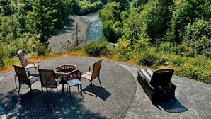 Ein Außenbereich mit Tisch und Stühlen mit Blick auf einen Fluss und bewaldete Berge.