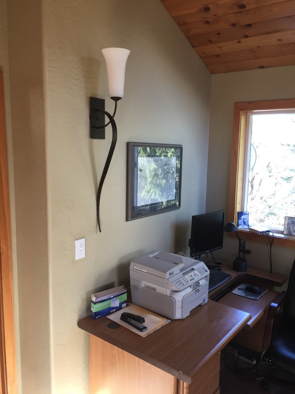 A home office with a desk, computer, printer, and a window with a view of trees.