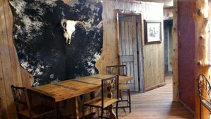 A rustic wooden interior with a large wall featuring a cow skull, a wooden table with chairs, and a wooden door.