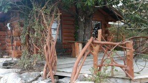 A rustic log cabin with a wooden deck, surrounded by rocks and trees.