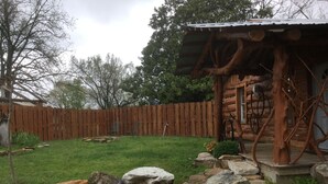 A rustic cabin with a wooden exterior, a porch supported by tree roots, and a surrounding wooden fence.