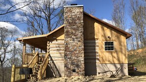 A rustic cabin with a stone chimney, wooden exterior, and a porch with a wooden railing. - HONEYMOON HIDEAWAY - SECLUDED ANTIQUE LOG CABIN WITH AMAZING VIEWS!!! (Gatlinburg)