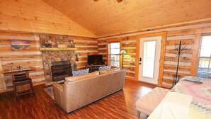 A log cabin interior with a fireplace, sofa, and a television. - HONEYMOON HIDEAWAY - SECLUDED ANTIQUE LOG CABIN WITH AMAZING VIEWS!!! (Gatlinburg)