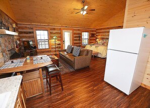 A cozy cabin interior with a wooden dining table, a sofa, a refrigerator, and a ceiling fan.