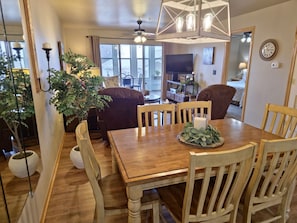 A dining area with a wooden table, six chairs, a chandelier, and potted plants.