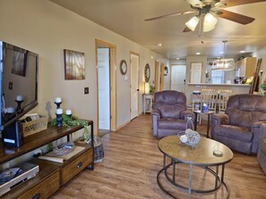 A spacious living room with a fireplace, leather armchairs, a coffee table, and a TV on a wooden cabinet.