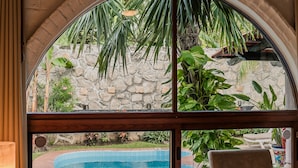 Camera da letto con un'ampia finestra ad arco che si affaccia su una piscina e rigogliosa vegetazione.