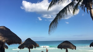 Una spiaggia con ombrelloni di paglia, lettini e una vista limpida sull'oceano.