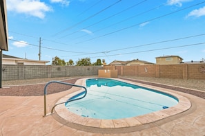 A swimming pool with a curved edge, surrounded by a brick wall and a paved deck.