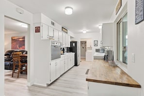 A modern kitchen with white cabinetry, a wooden countertop, and a dining area with a leather sofa and wooden chairs.