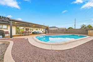 A residential backyard with a swimming pool, patio furniture, and a covered outdoor seating area.