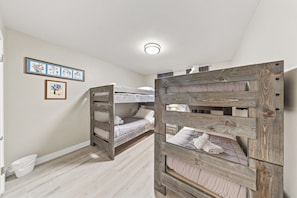 A room with two bunk beds, a white ceiling, and a light fixture. There are framed pictures on the wall.