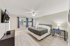 A hotel room with a bed, a desk, a chair, a television, and a ceiling fan.