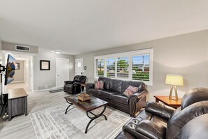 A living room with a leather sofa, a coffee table, and a TV mounted on the wall.