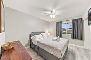 Une chambre à coucher avec un lit, une table de chevet, un ventilateur de plafond et une fenêtre avec des rideaux.