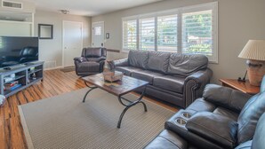A living room with a leather sofa, a coffee table, a television, and a window with blinds.