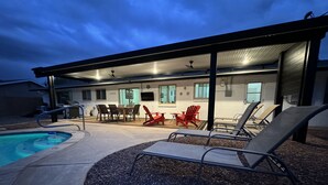 A covered outdoor area with a pool, lounge chairs, and a dining table.