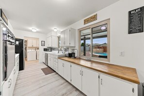 A modern kitchen with white cabinetry, a wooden countertop, and a view of a swimming pool through a large window.