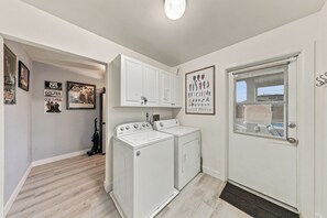 Une buanderie équipée d’un lave-linge et d’un sèche-linge, une porte avec une fenêtre et divers objets encadrés accrochés au mur.