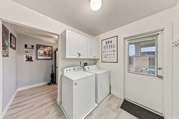 A laundry room with a washer and dryer, a door with a window, and various framed items on the wall.